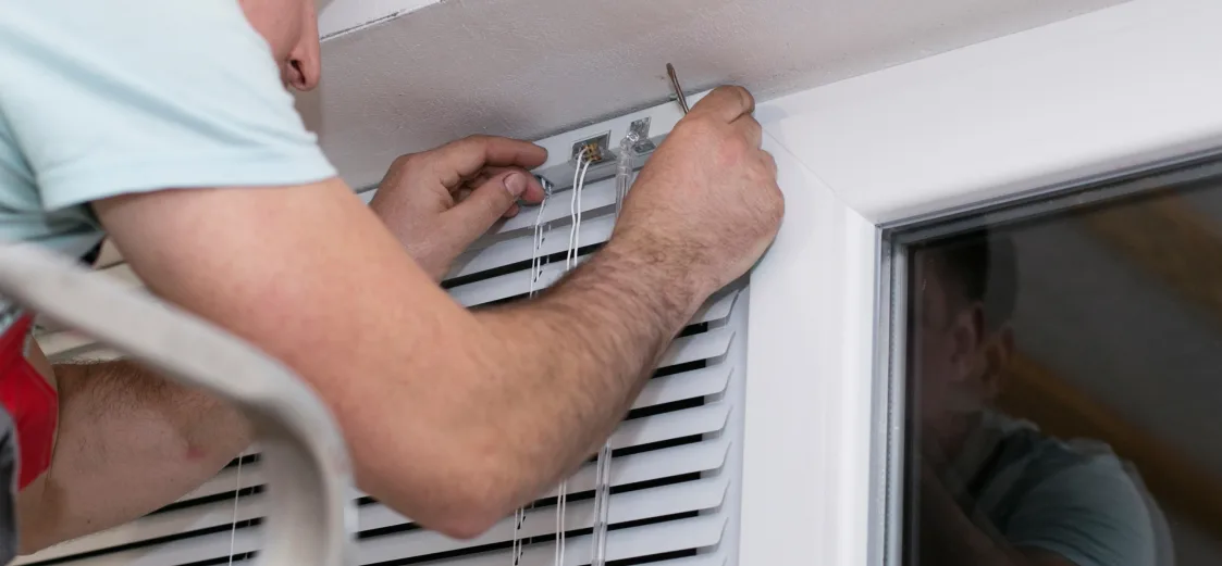 Someone fixing blinds while standing on a step ladder