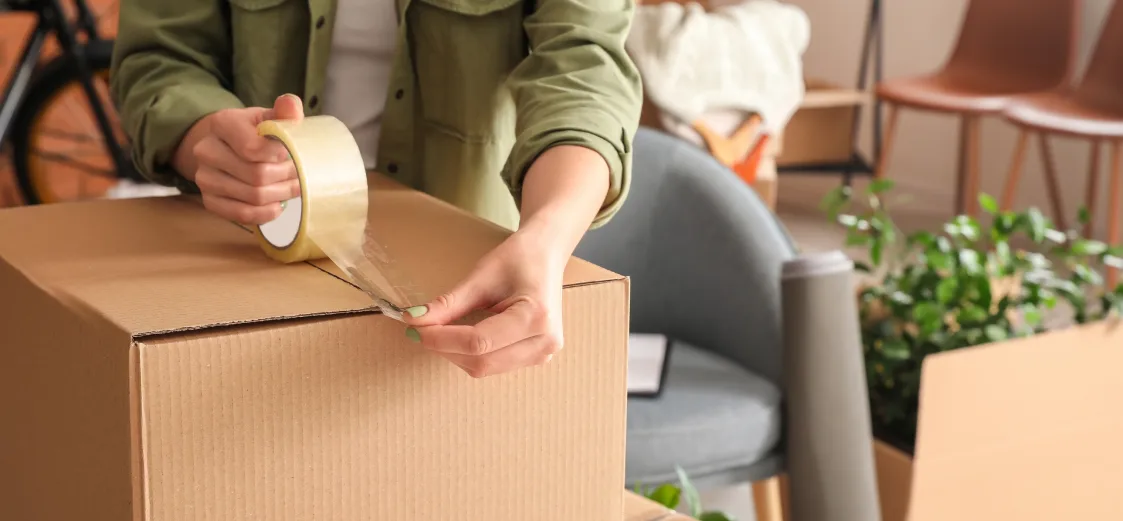 A picture of someone sealing a moving box with packing tape. 