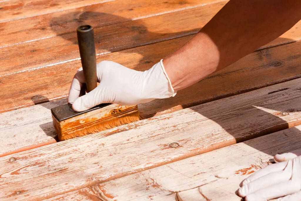 A picture of someone staining and resurfacing an deck.