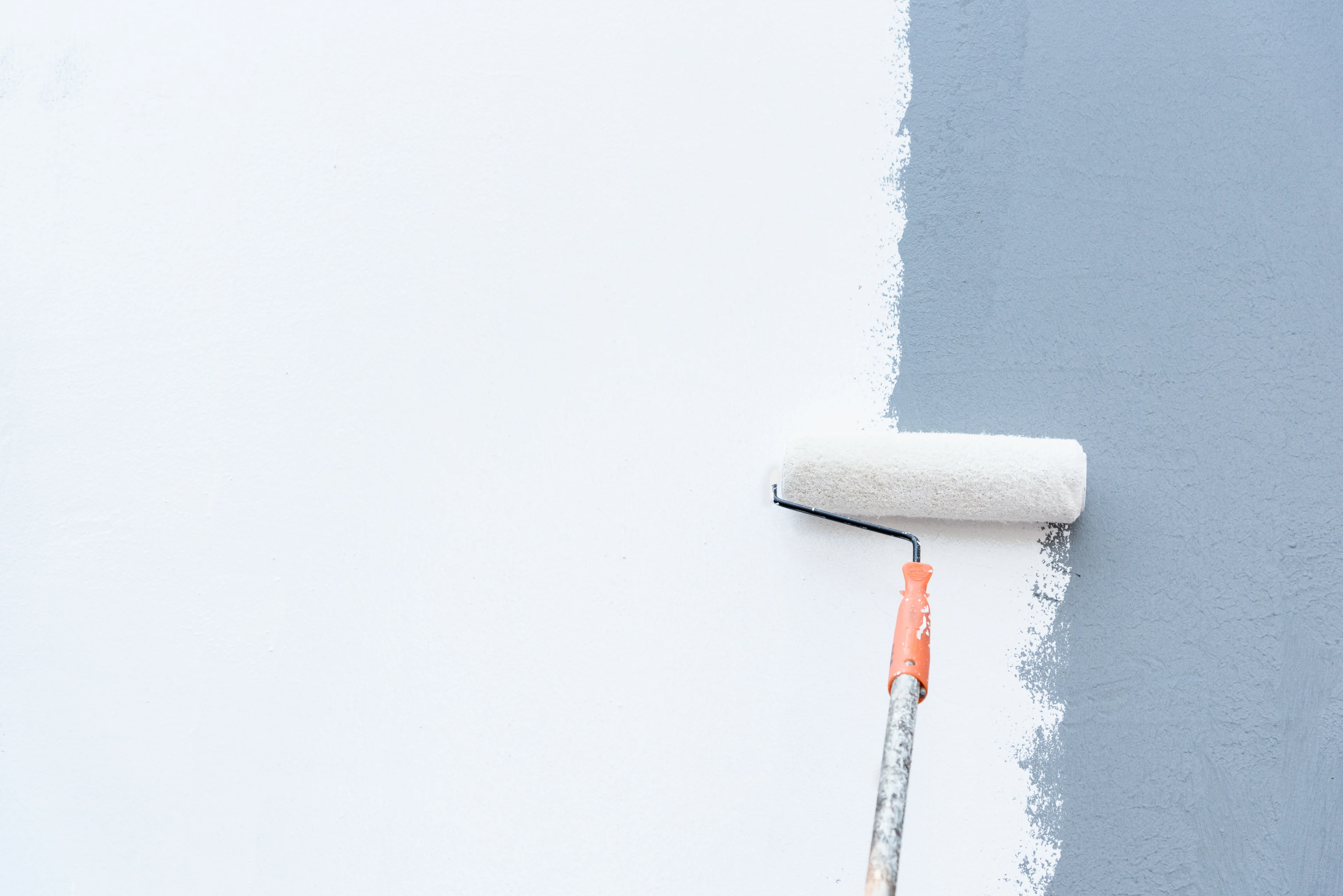 a paint roller painting a grey wall white