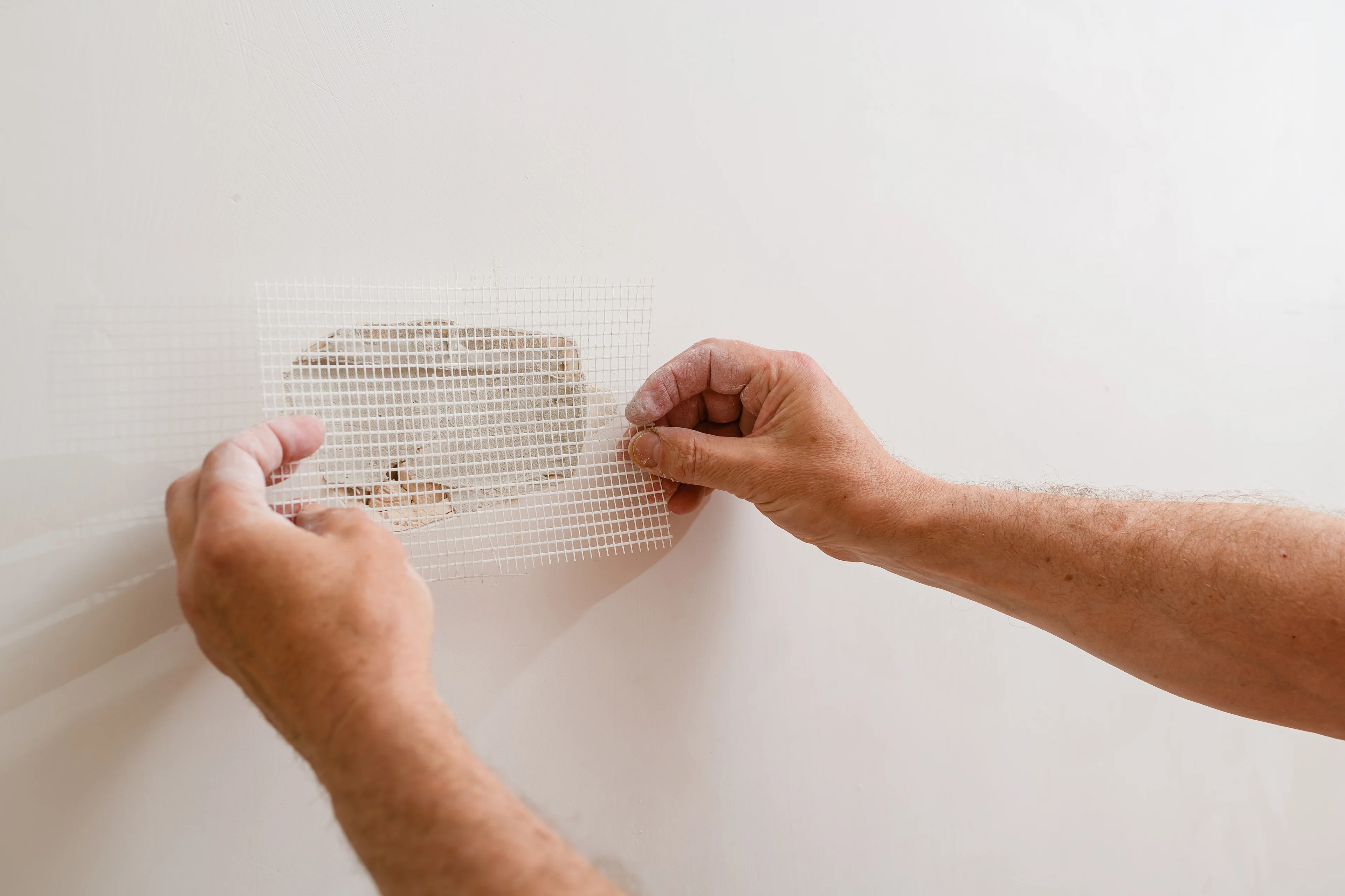 a person placing a drywall patch over a hole in a wall. 