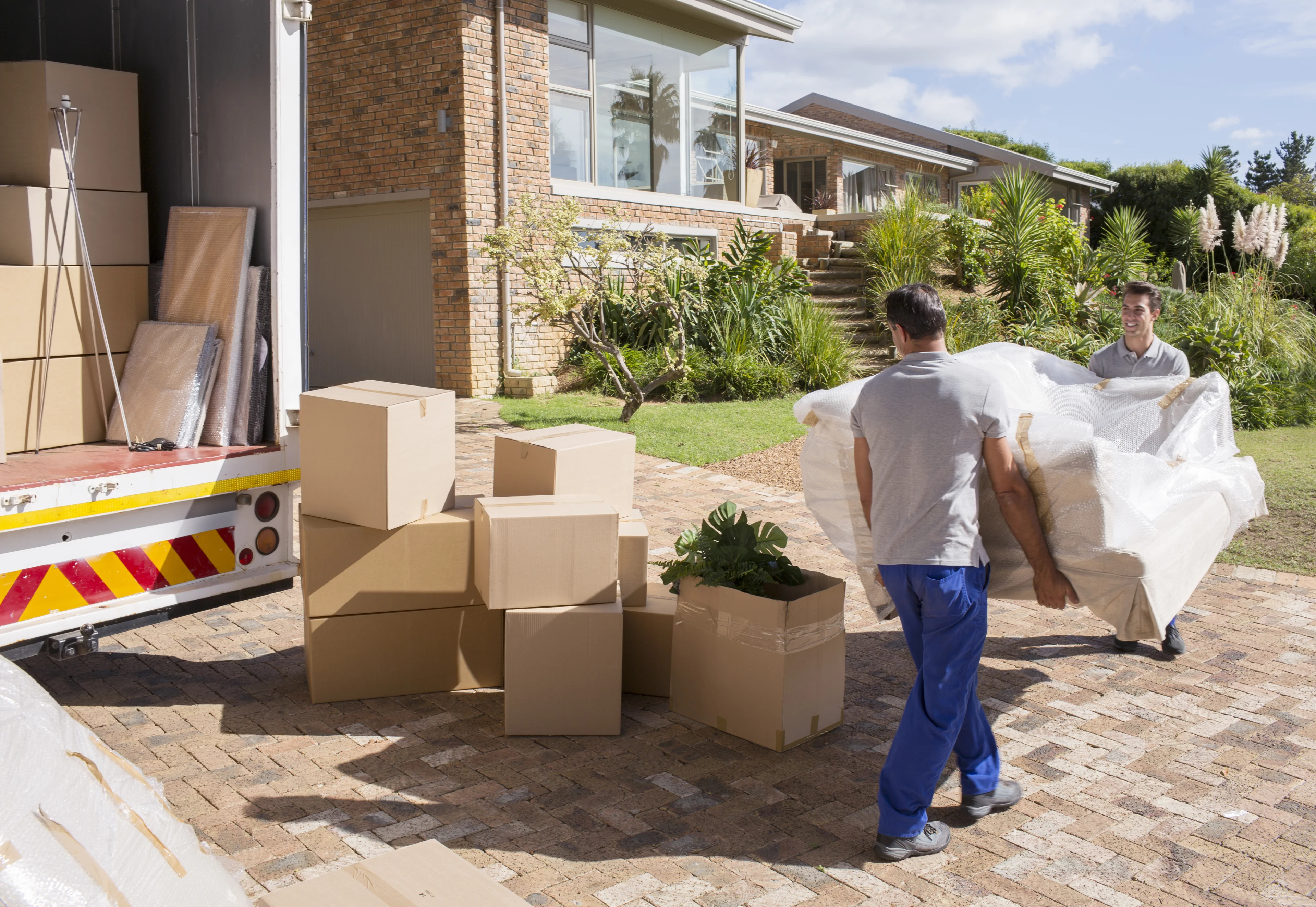 two men moving a couch into a house from a moving truck. 