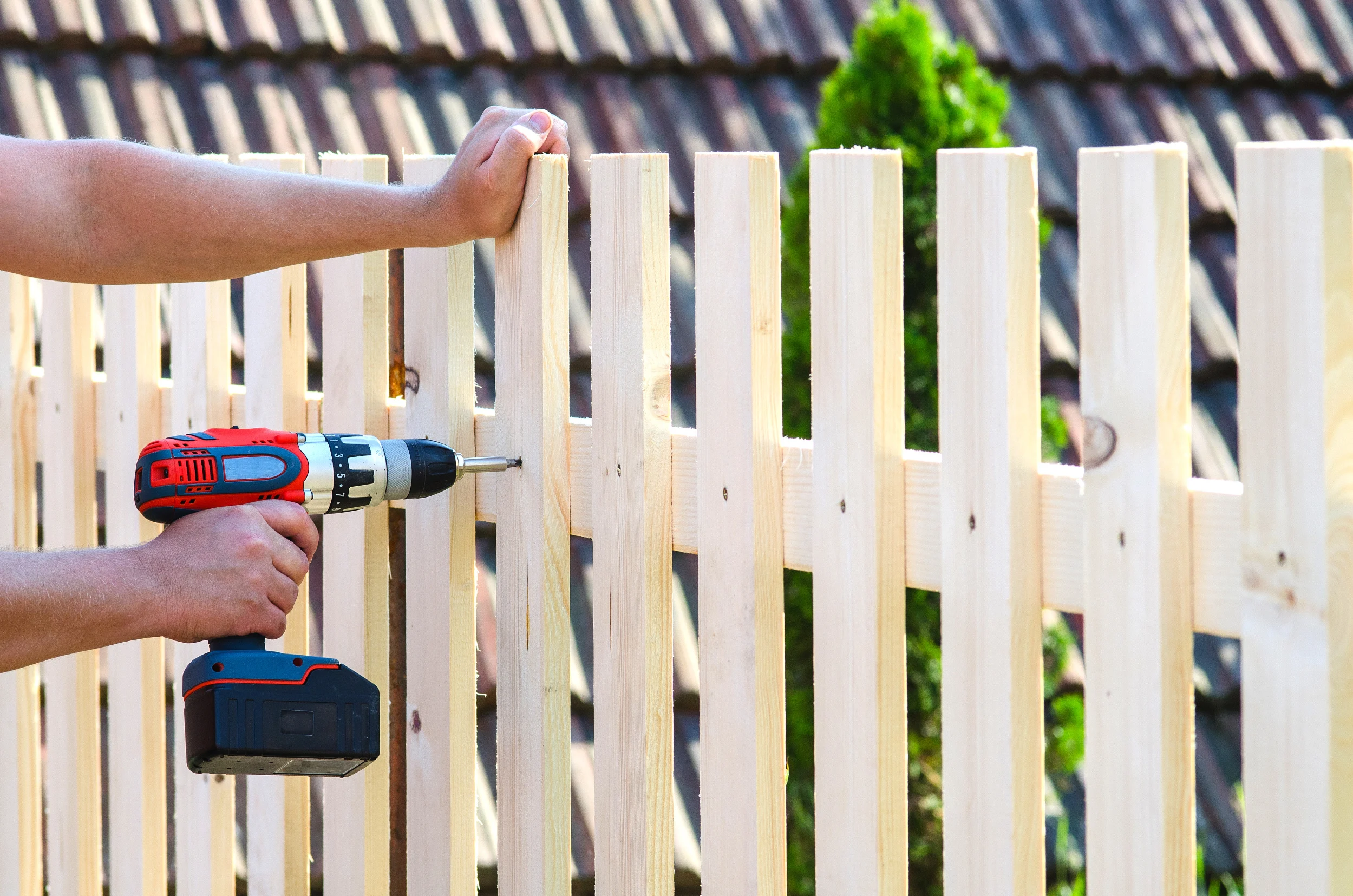 a person installing a fence and drilling a screw into a fence post. 