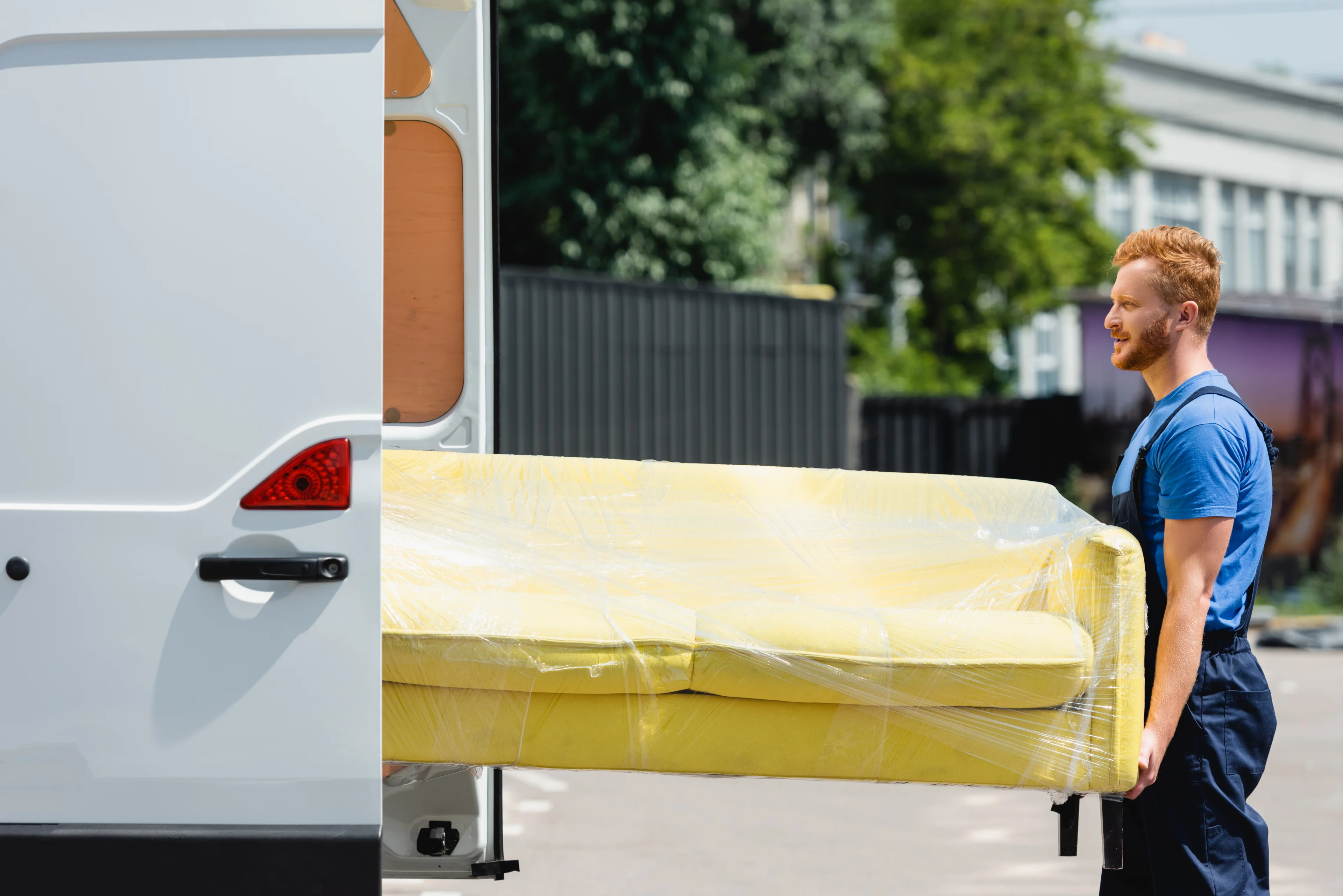 a person help move a plastic covered couch into a transit van. 