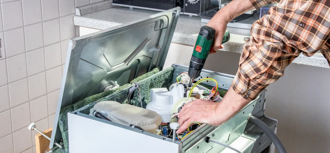 A picture of someone fixing a washing machine with a drill. 