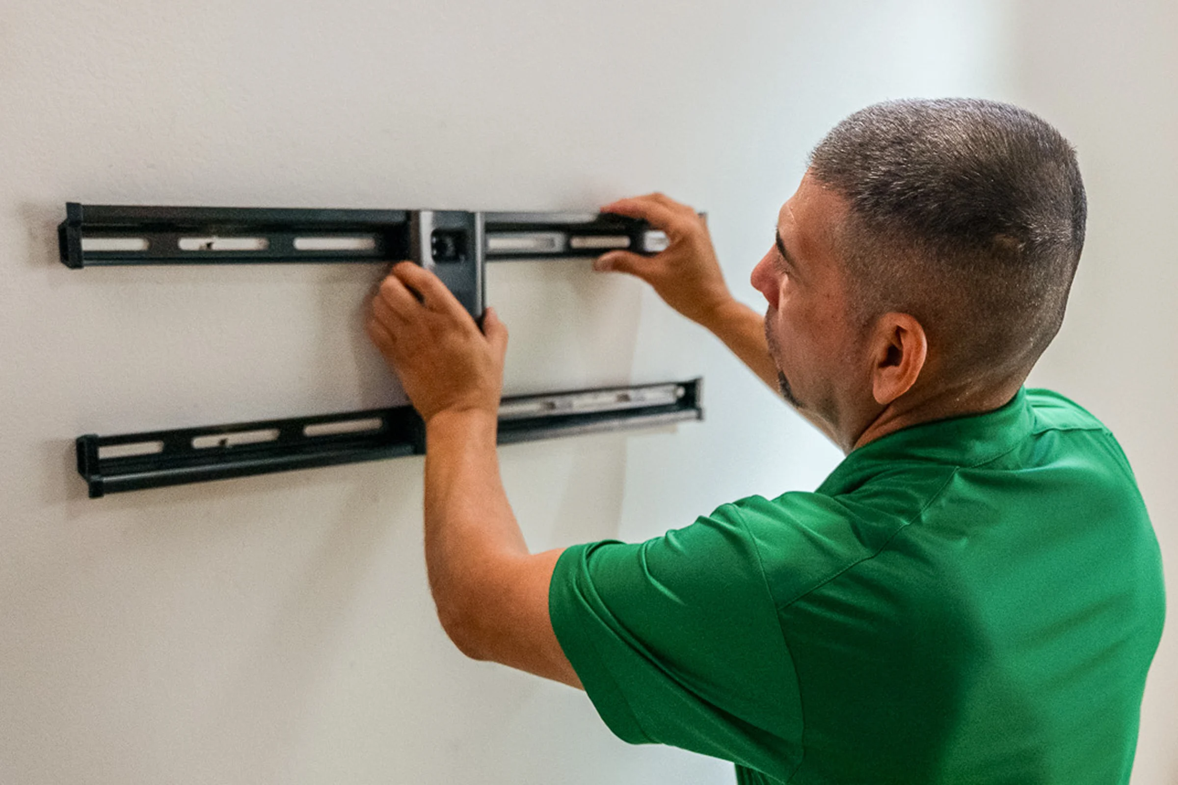 une personne installant un support TV extensible au mur avec un téléviseur qui y est fixé. 
