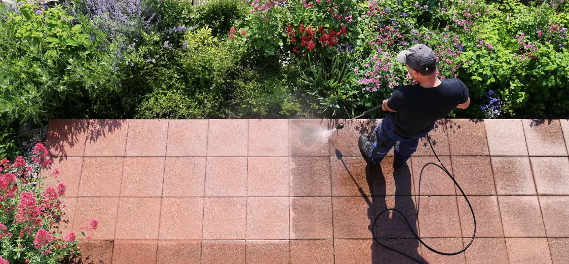 An image of someone pressure washing a stone walkway in a garden. 