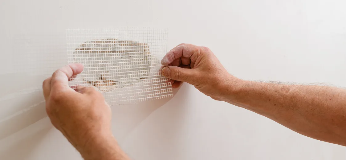 A picture of someone patching drywall with mesh