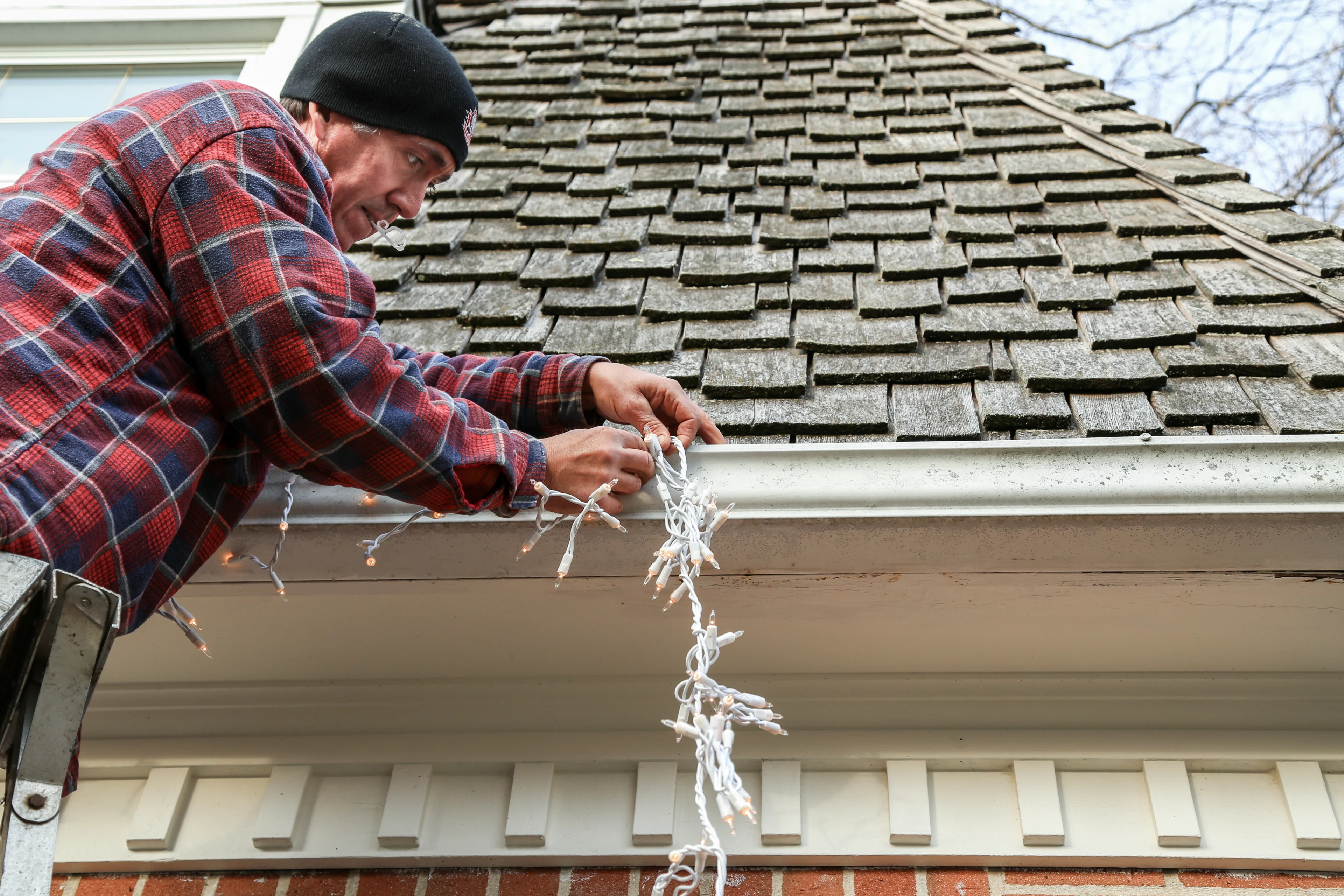 a person hanging christmas lights on the roof of a house. 