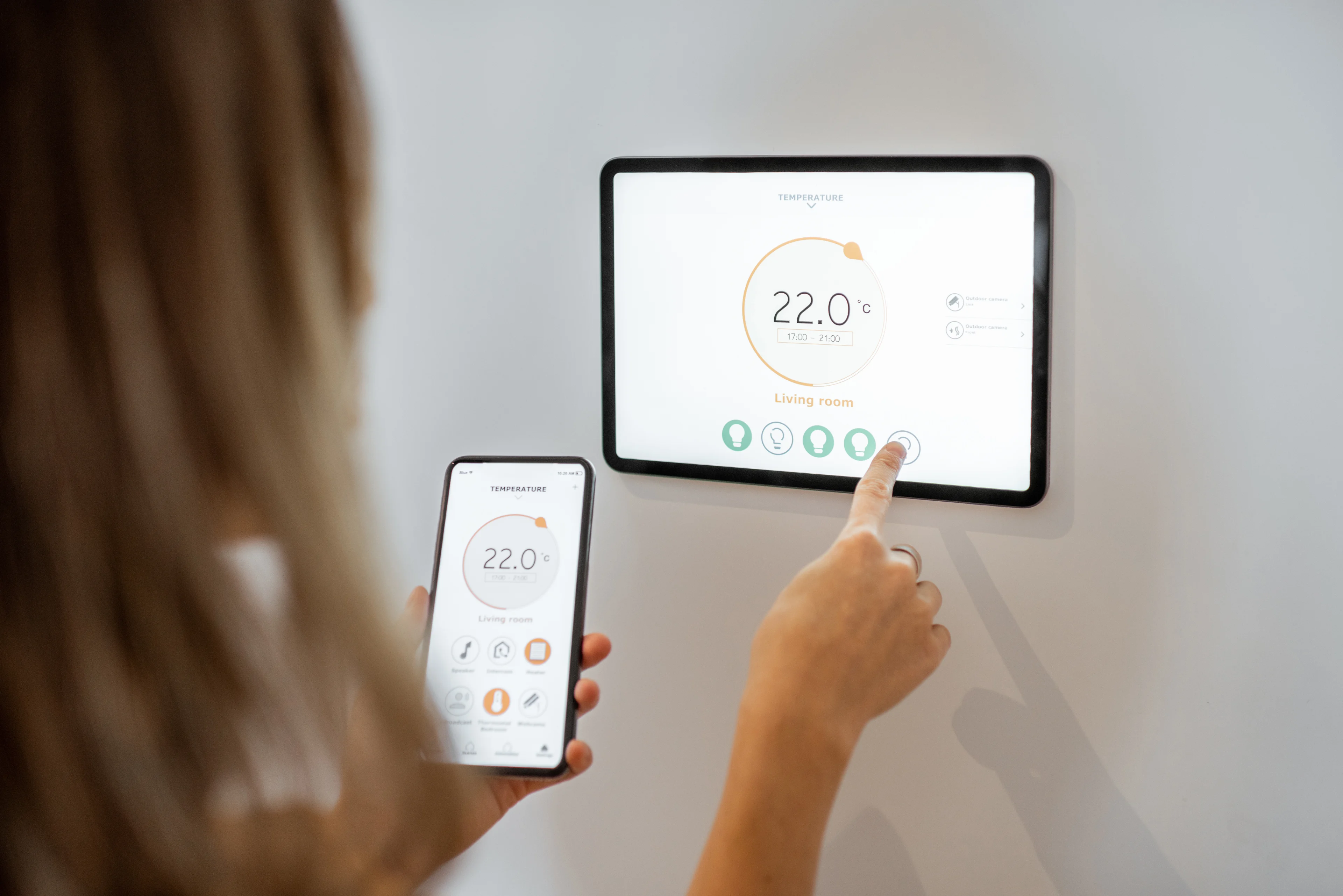 a woman using a smart thermostat to set the temperature in her home. 