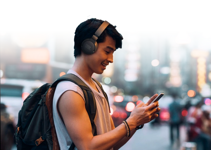Une personne souriante écoute de la musique avec des écouteurs sans fil et utilise un téléphone intelligent sur la rue.
