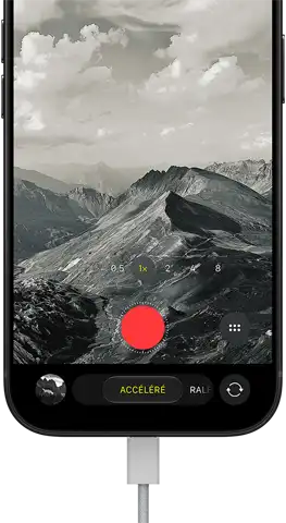 Un iPhone 18 Pro, face avant, affichant un paysage montagneux, avec le menu superposé du mode caméra en mode accéléré, câble d’alimentation branché au port de recharge