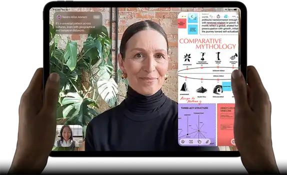 iPad Pro, front exterior, landscape orientation, space black colour, rounded corners, black display bezel, hands holding left and right sides, display showing a FaceTime conversation being live translated, and an educational app showing a presentation of "Comparative Mythology" with text, diagrams and handwritten notes