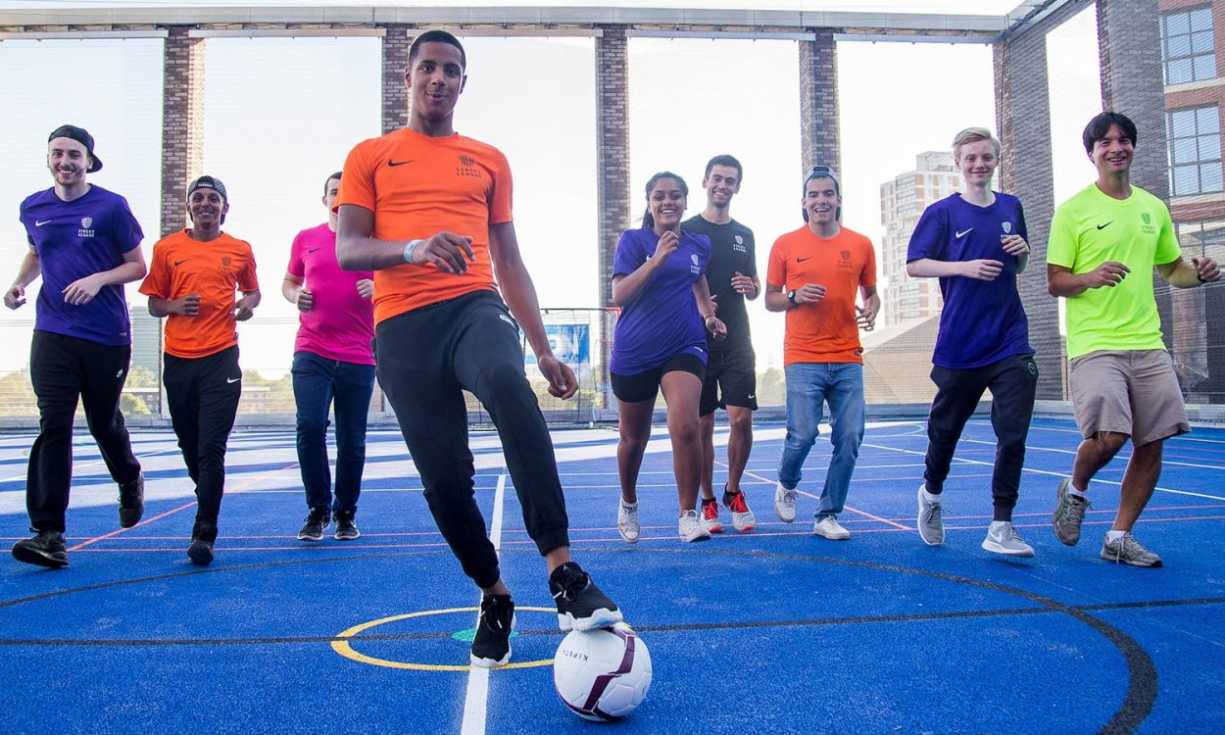 Nine participants wearing Street League t-shirts jog on an artificial football pitch