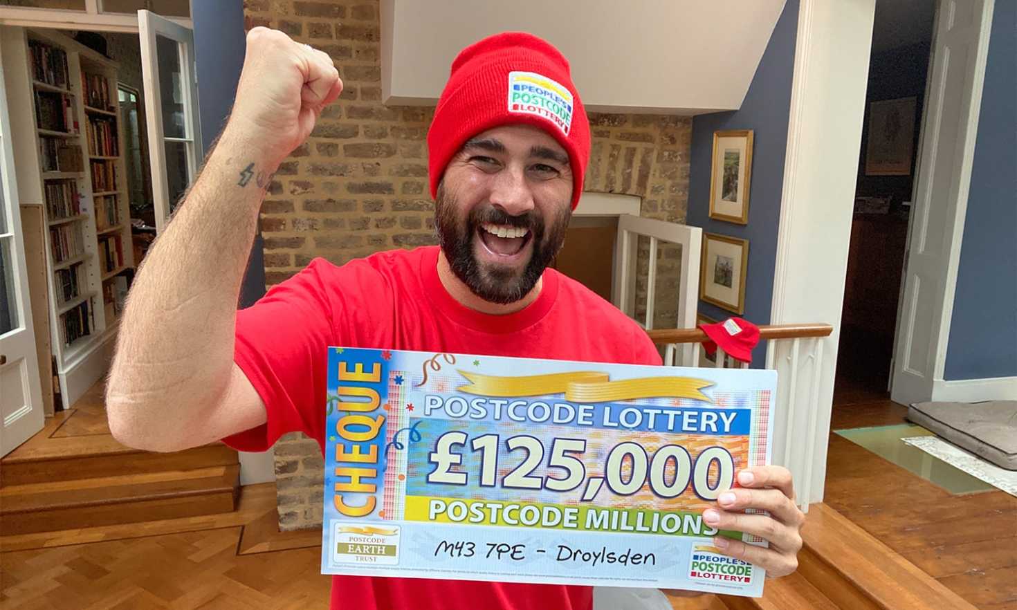 Matt punches the air as he reveals one of our big Postcode Millions winner cheques