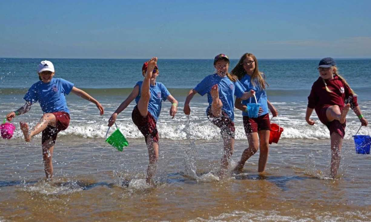 Five young people holding buckets and spades enjoy themselves on a beach