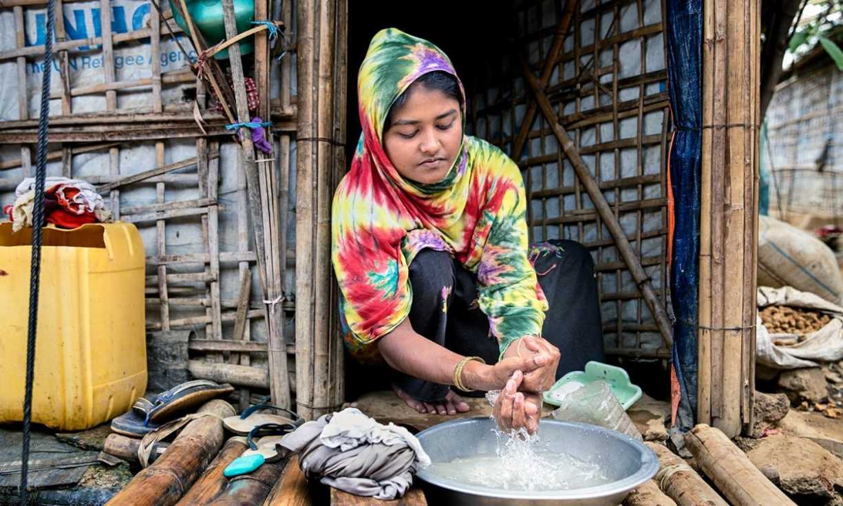 Hafeza cleaning her hands at the doorstep of her tent during the COVID 19 outbreak in the Rohingya Refugee Camp in Cox's Bazar, Bangladesh