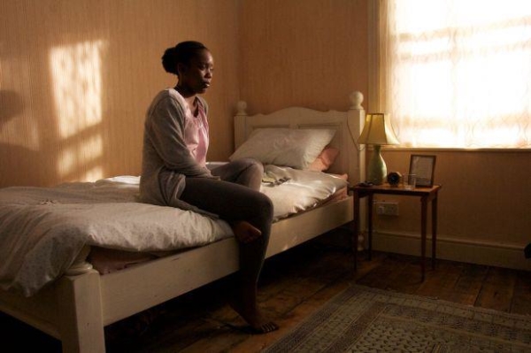 A solitary woman sitting on a bed in a room by a window.