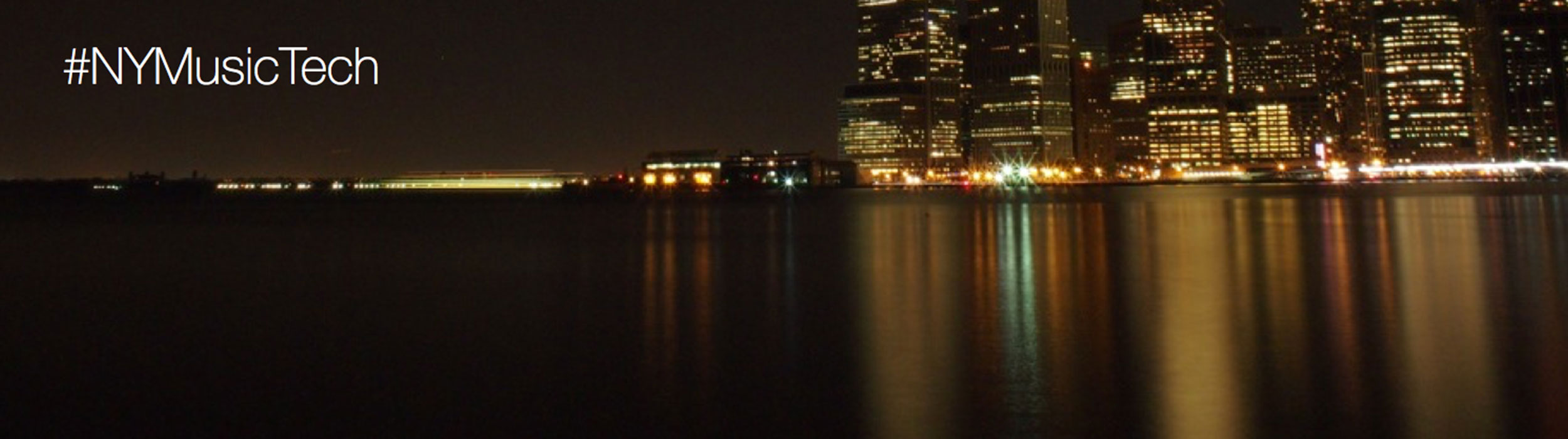 A nighttime view of New York over the Hudson river with the #NYMusicTech hasthatg.