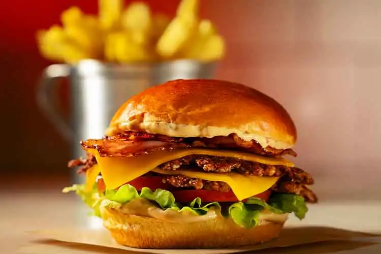 Hamburguer suculento de bacon e queijo cheddar acompanhado por batatas fritas.