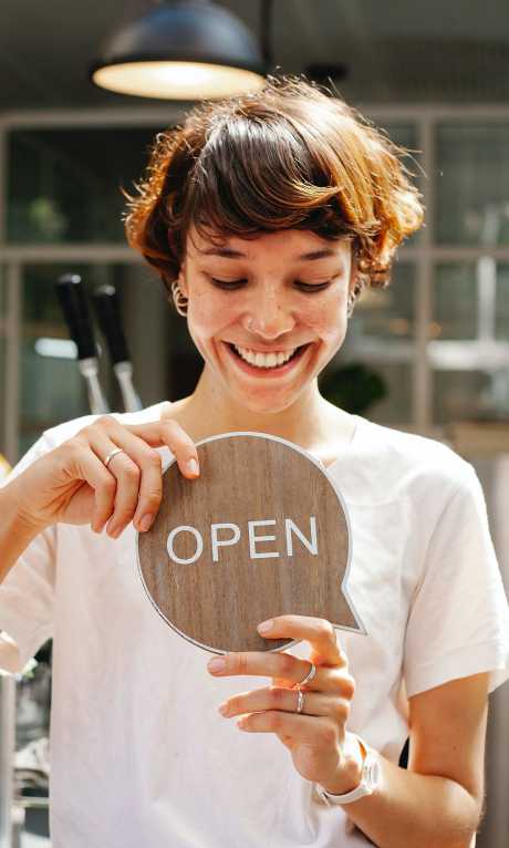 Flicka står och håller en skylt i handen som säger Öppna