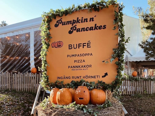 Utomhusskylt för buffén "Pumpkin n' Pancakes" med pumpor i botten och menyalternativ: pumpasoppa, pizza, pannkakor samt vägbeskrivning på svenska.