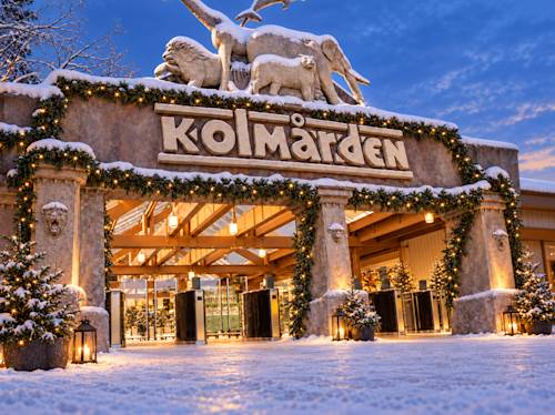 Ingången till Kolmårdens djurpark är dekorerad med girlander och ljus på vintern, med djurstatyer på toppen och snö som täcker marken och byggnaden.