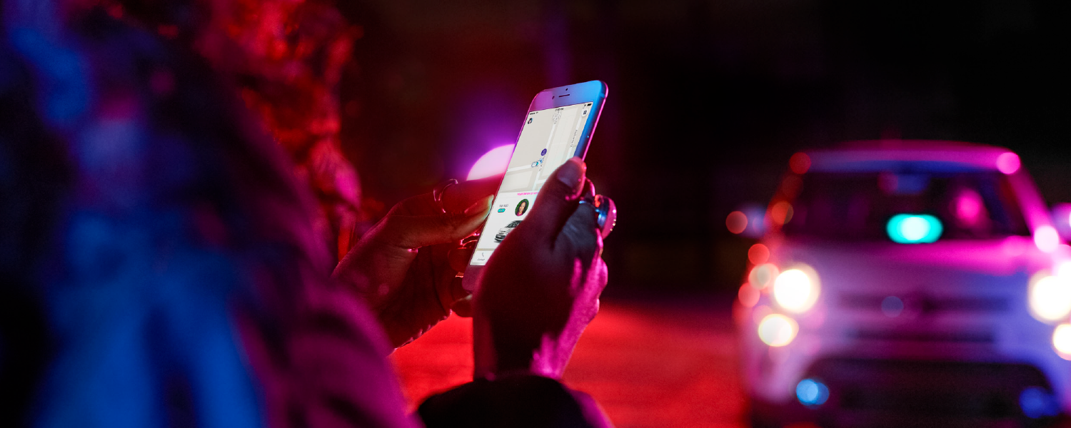 A passenger looking at their phone and waiting while their Lyft arrives with a green AMP visible in the windshield.