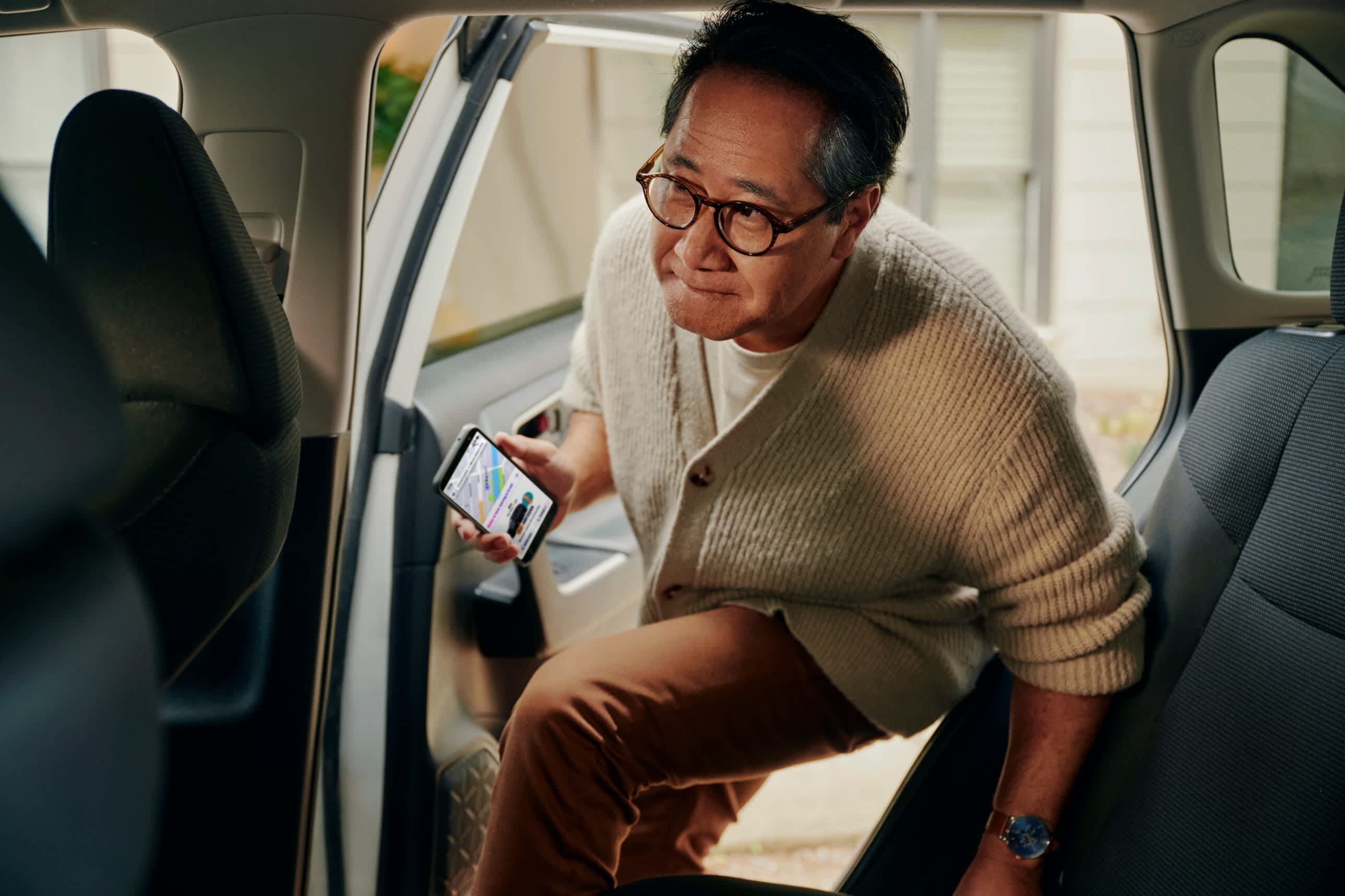 Older man getting inside the back of a car holding mobile phone