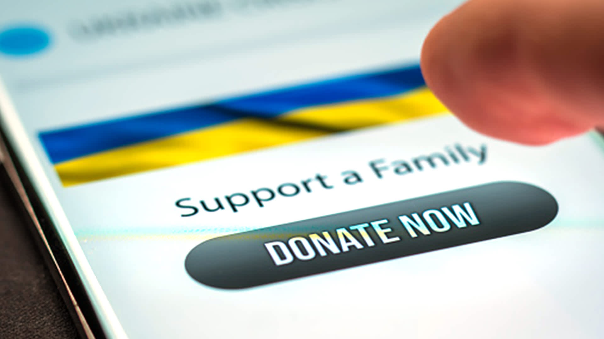image of a finger hovering over a mobile phone showing the Ukrainian flag with the the text Support a Family and a Donate Now button  
