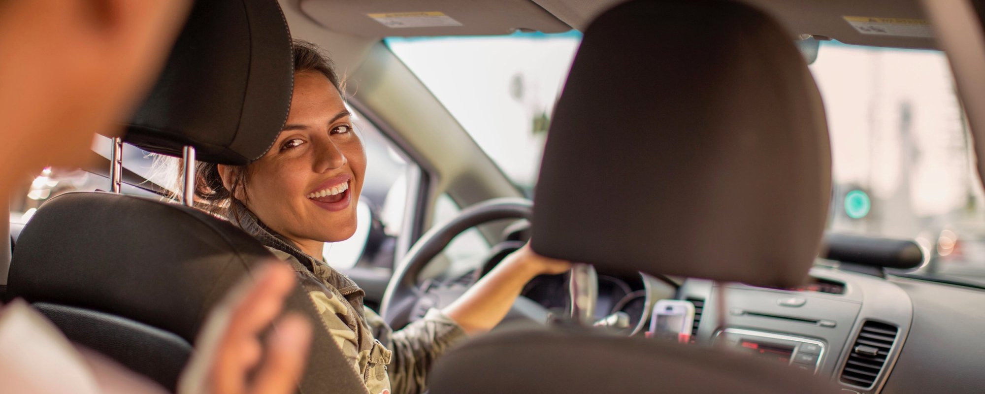 A female Lyft driver smiling back at her passenger.