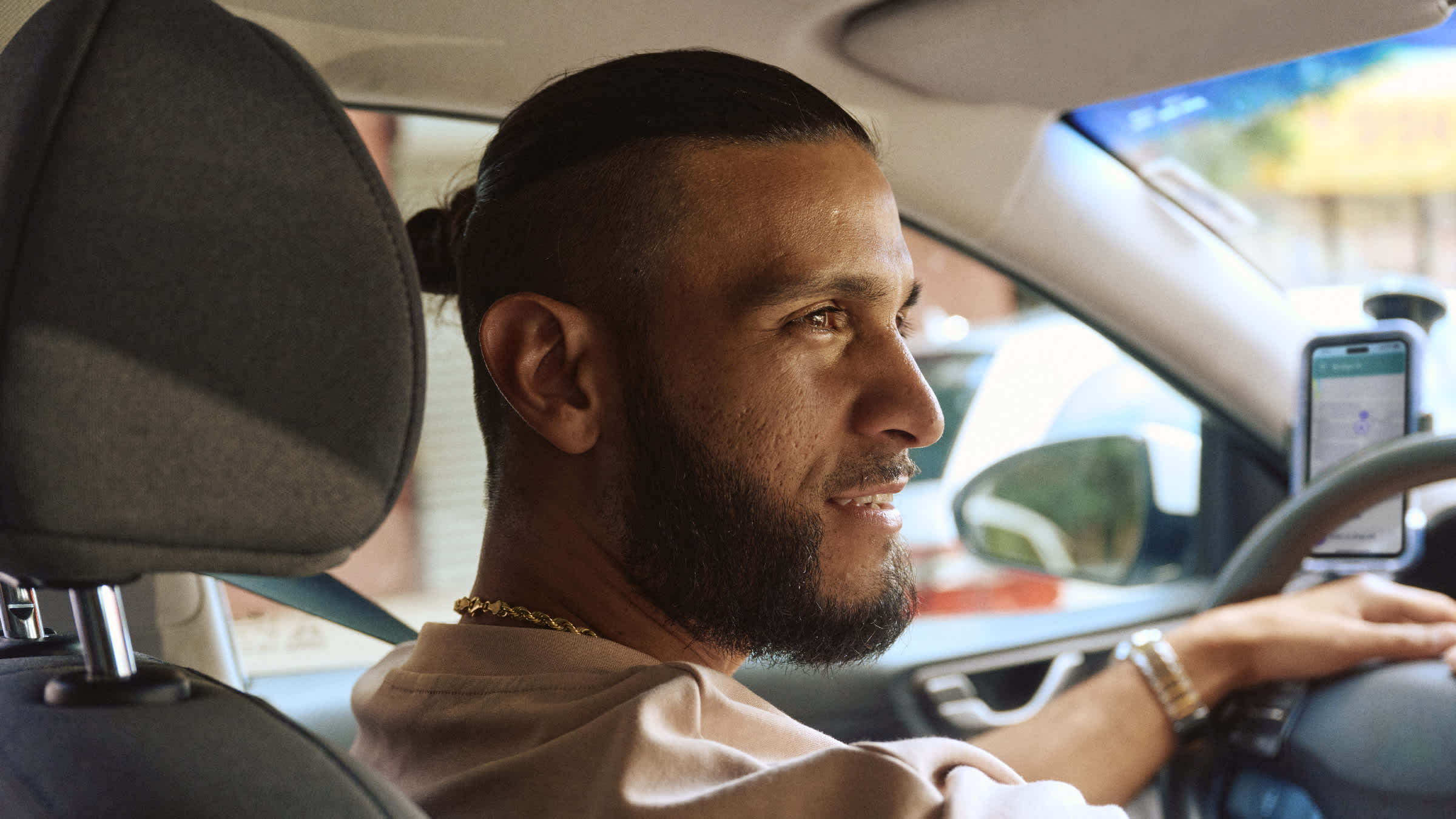 Driver in driver's seat with smartphone mounted on dashboard, wearing beige clothing.