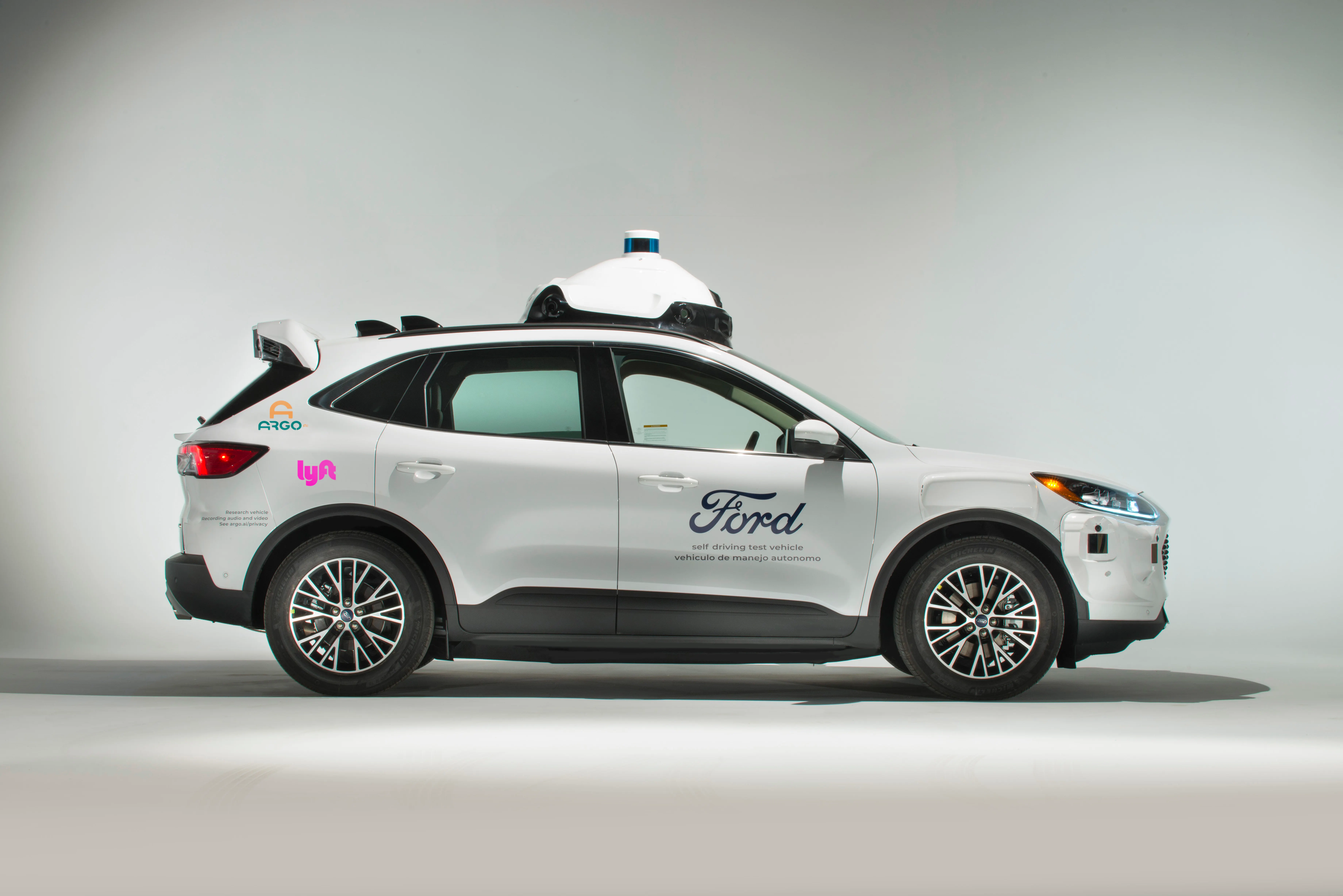White Ford Escape test vehicle with Argo and Lyft logos and roof-mounted sensors