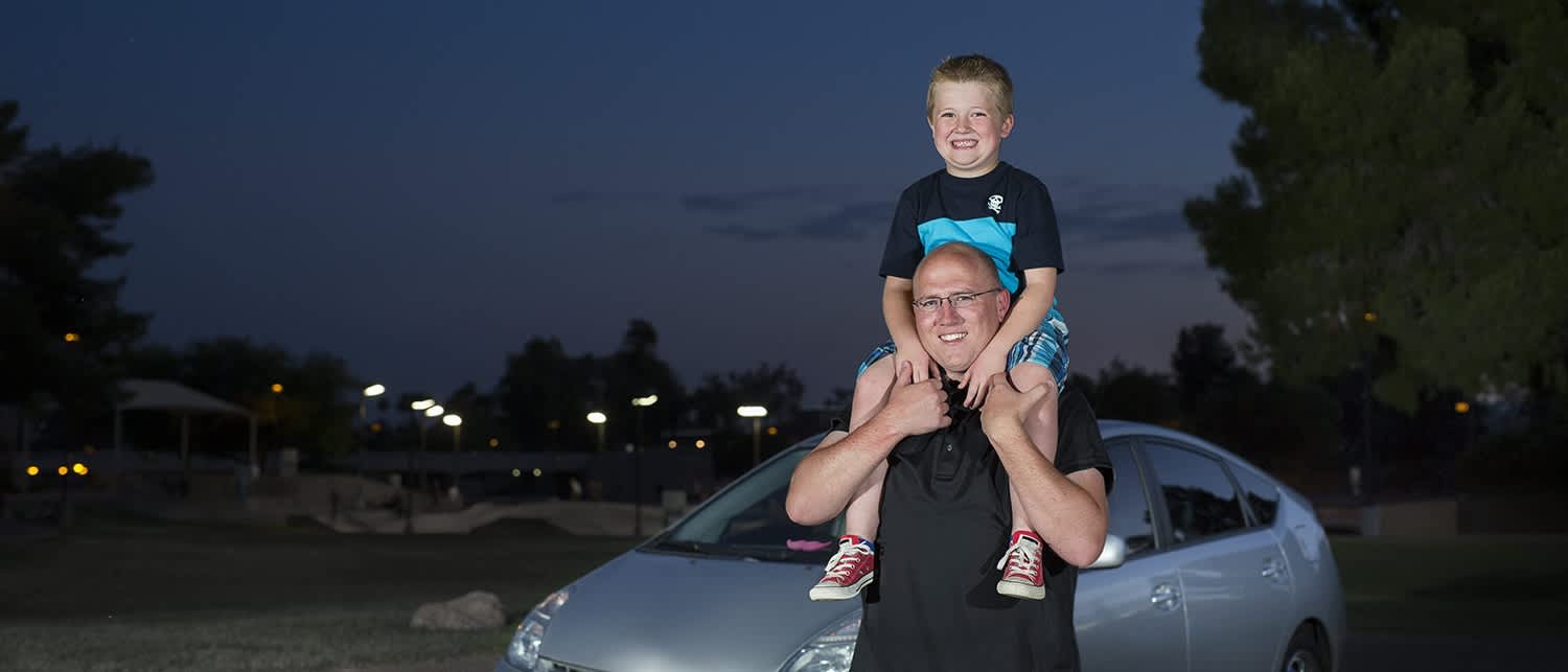 Gene and his son standing in front of his car.