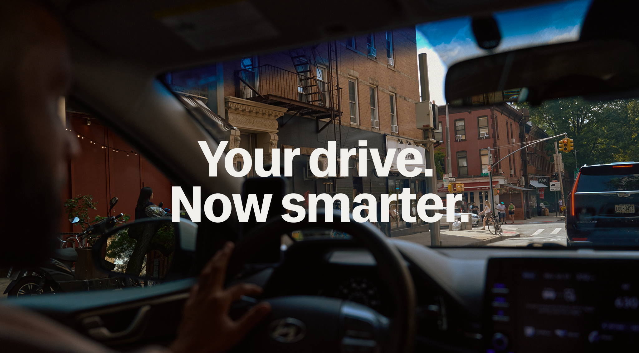 View from inside a car driving through a city street with text overlay reading "Your drive. Now smarter."
