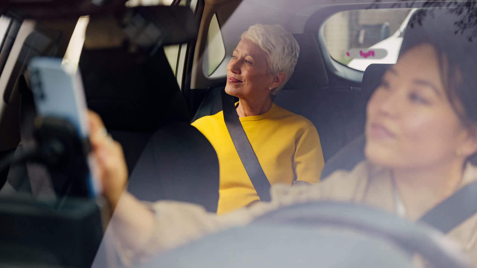 Passenger in bright yellow top smiling in a car with Lyft logo visible in the window.
