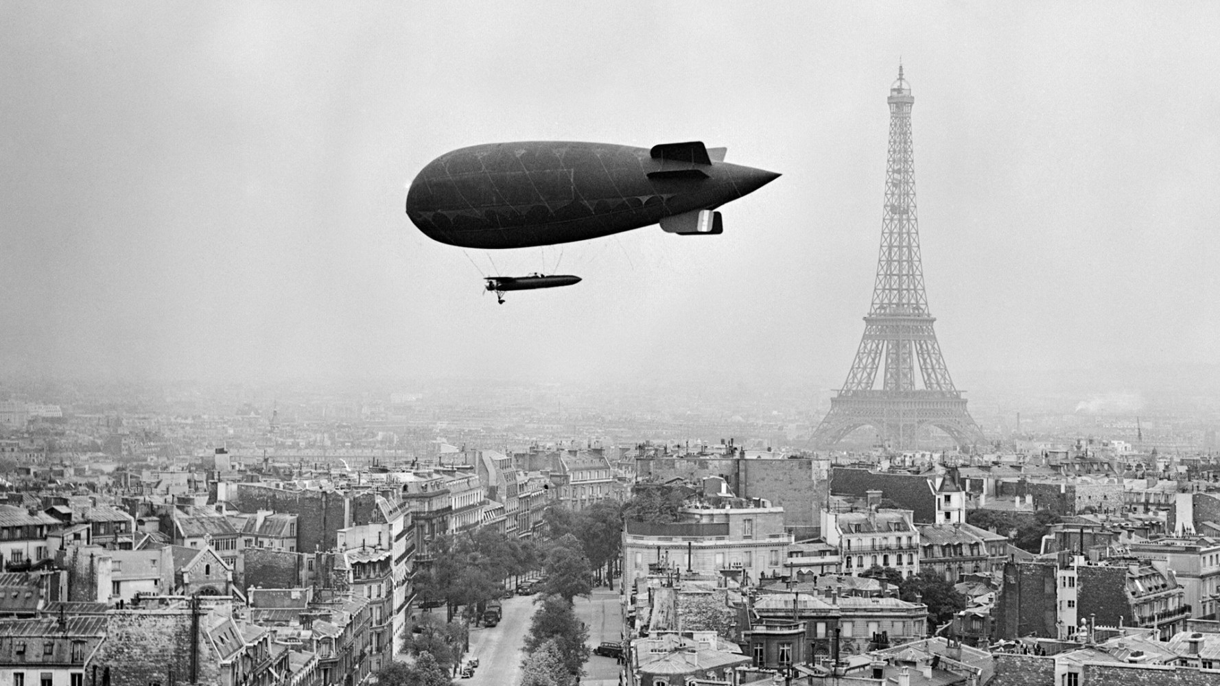 An airship flying above Paris, with the Eiffel Tower dominating the skyline.