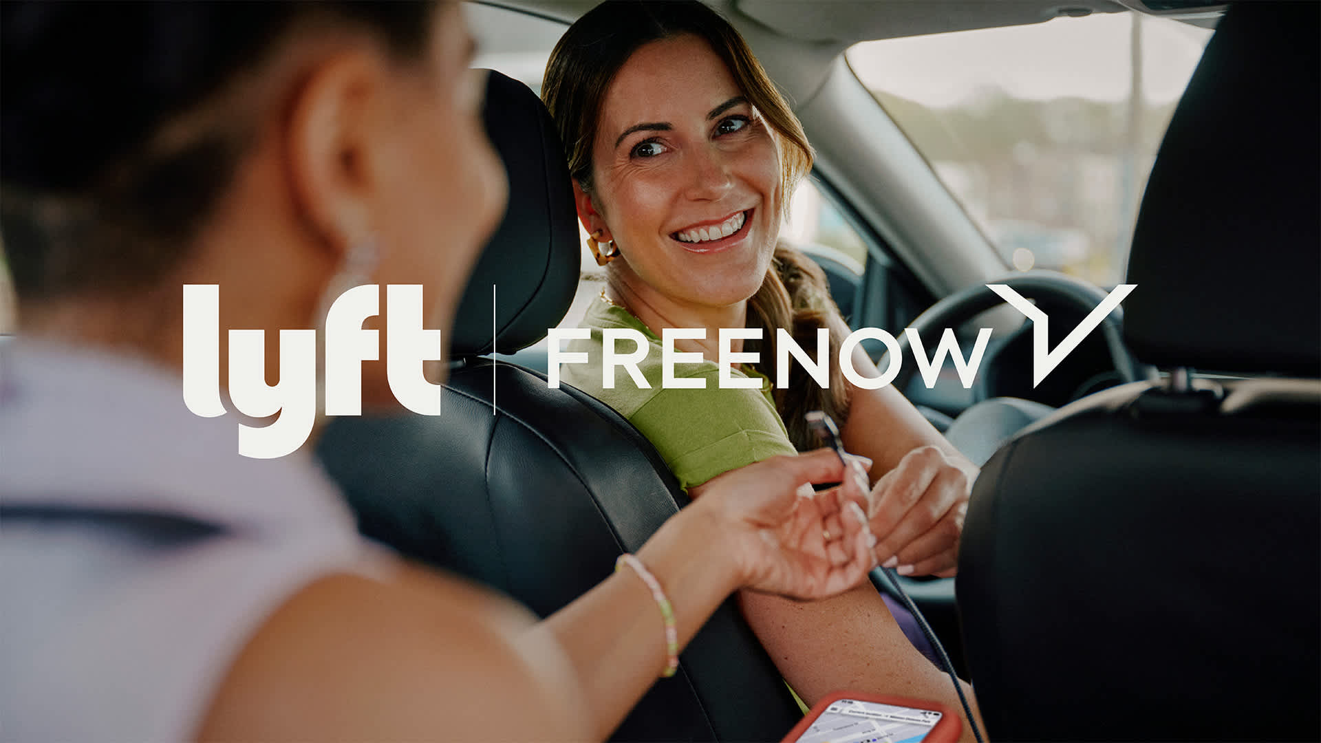 Smiling driver in car with passenger, Lyft and FREENOW logos displayed on the image.