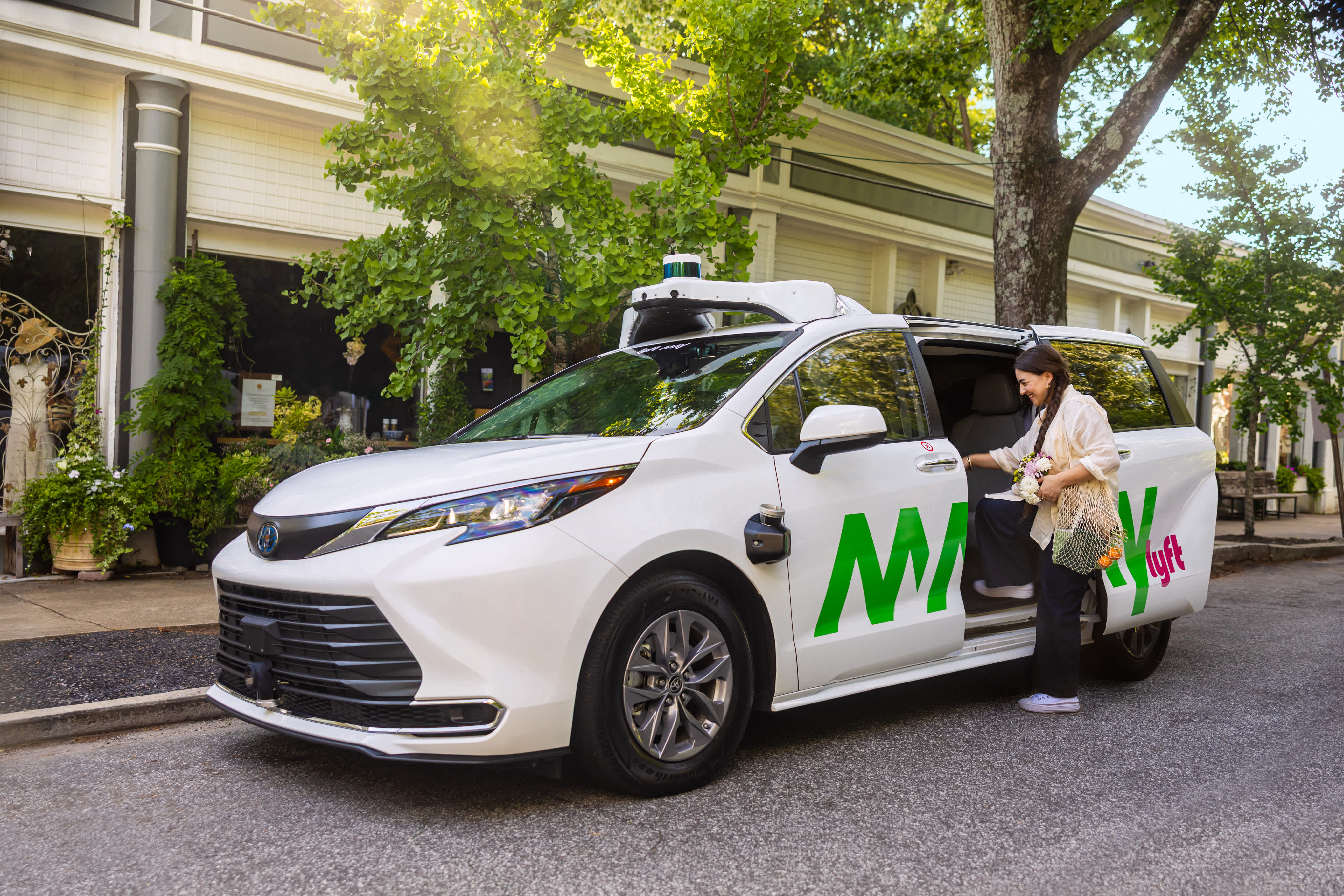 Passenger entering a white Lyft May Mobility autonomous vehicle. 