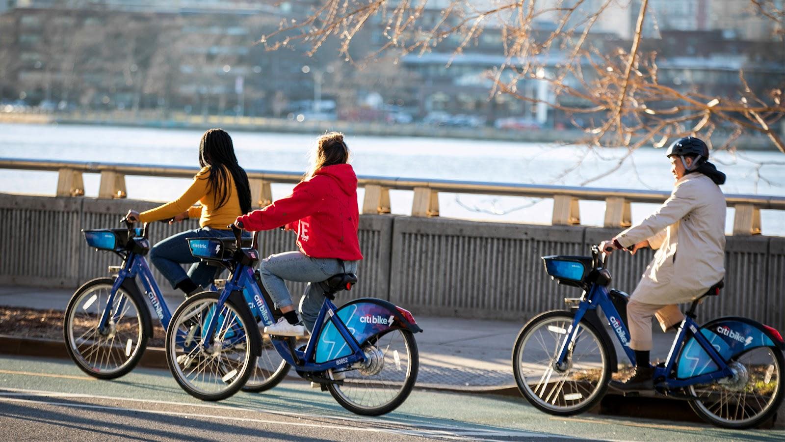 Photograph of three cyclist riding Citibike bike-bikes on a bike path along the Hudson River in New York City.