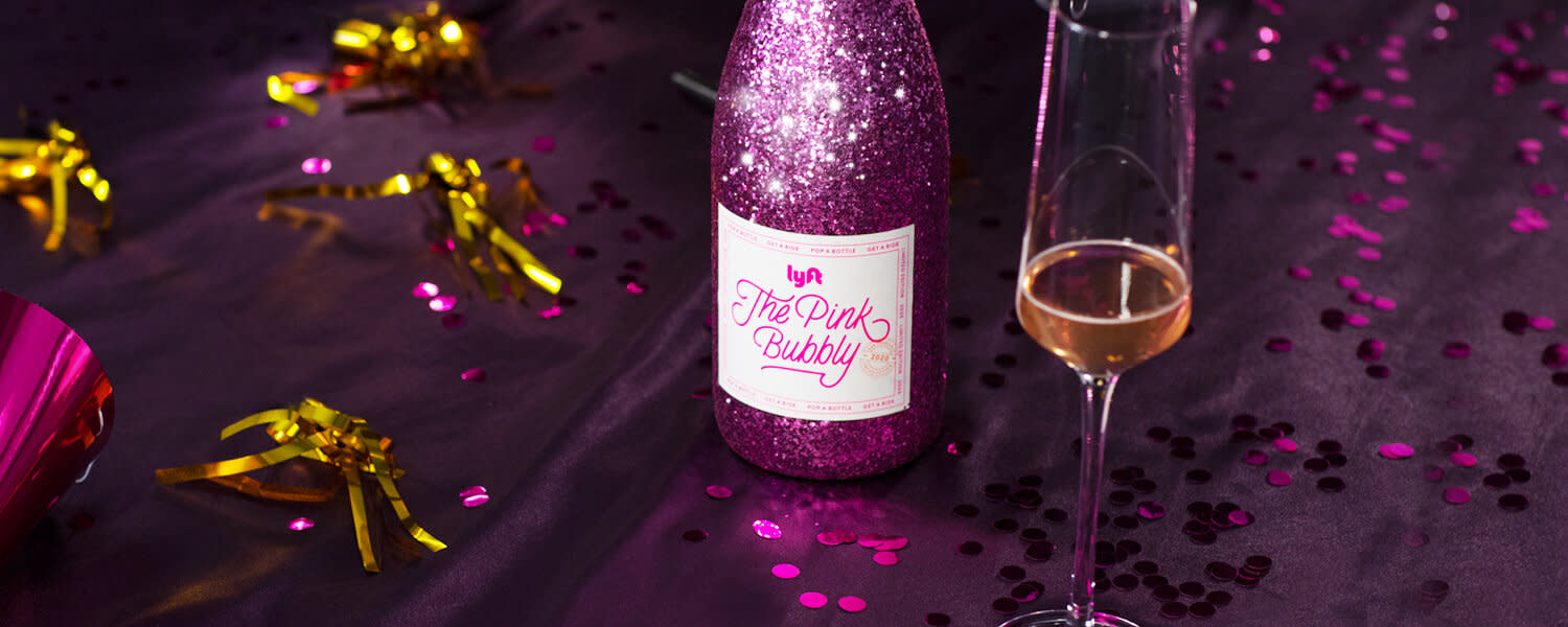 A bottle of Lyft "The Pink Bubbly" champagne with a champagne flute and confetti.
