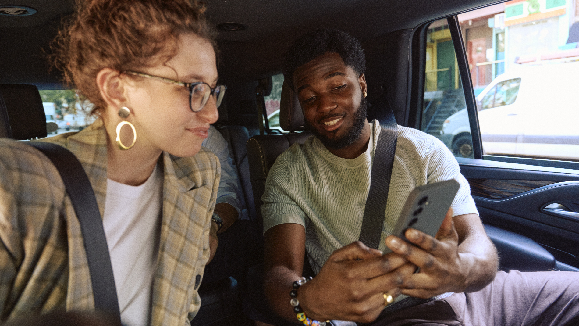 Two passengers sharing a smartphone screen in the backseat of a car. 