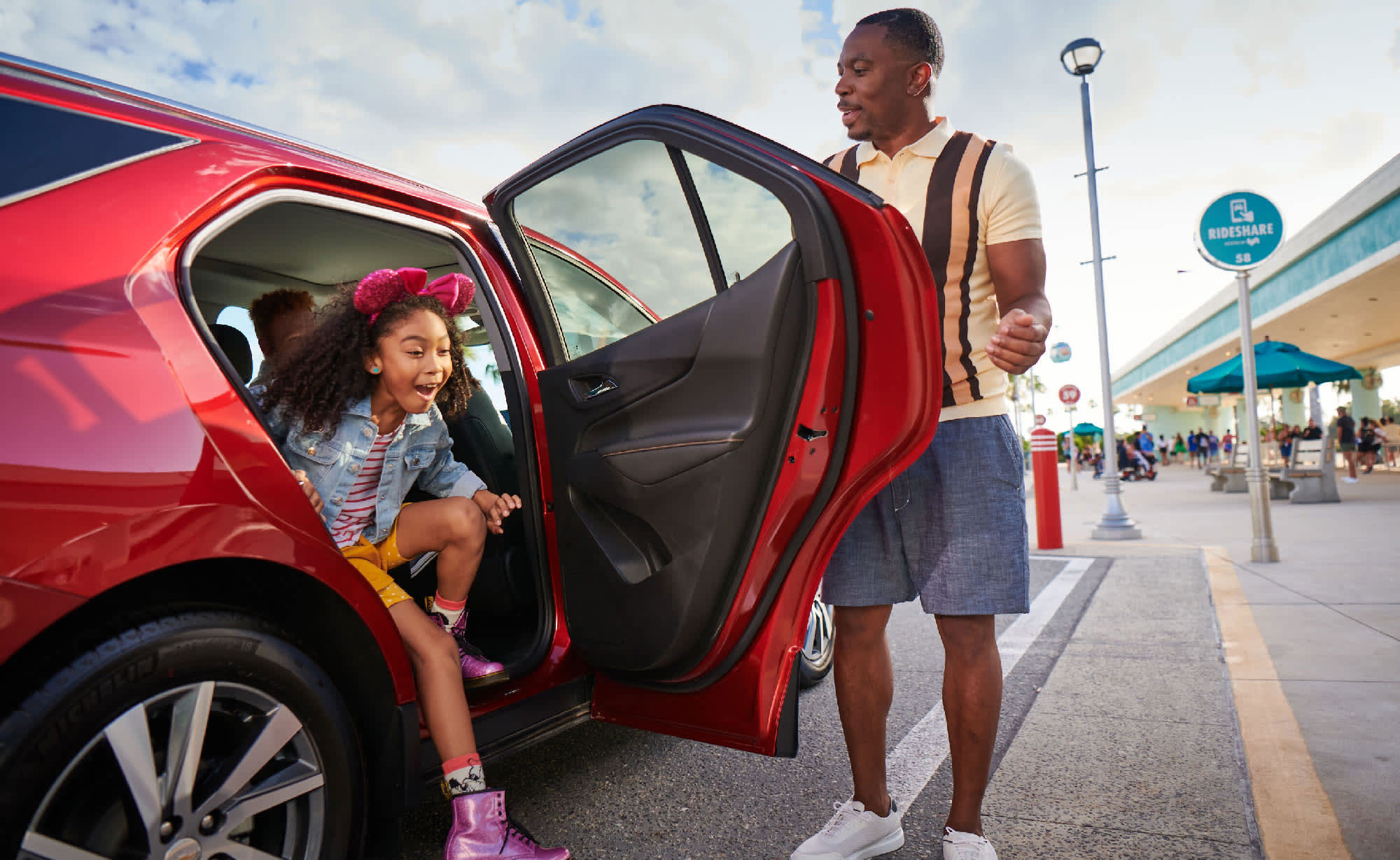 Excited girl exits a red car at a Disneyland Resort pickup zone as a man opens the door.