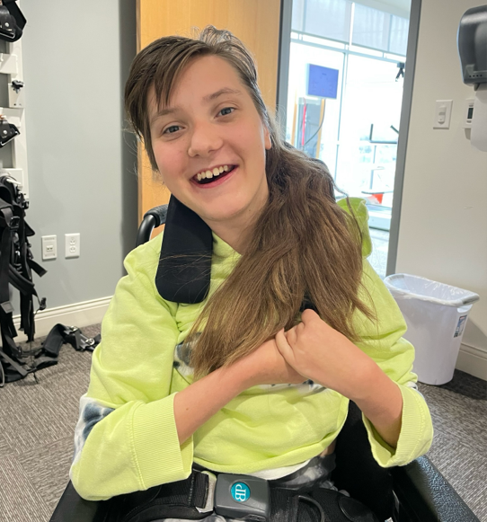 Child living with Rett syndrome at 10+ years old holding her hands and smiling