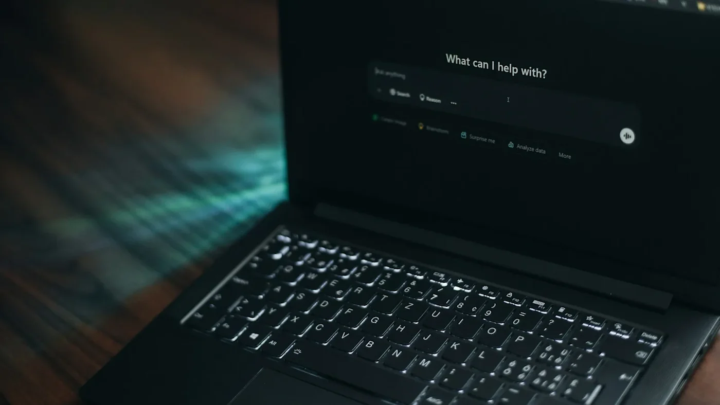 A laptop on a wooden table showing an AI assistant asking what it can help with