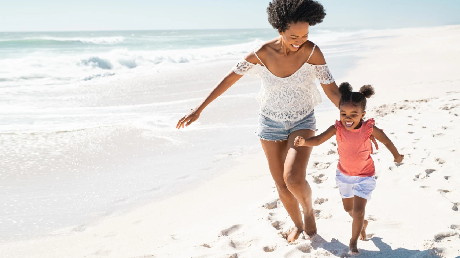 Mother and daughter smiling and running on the beach