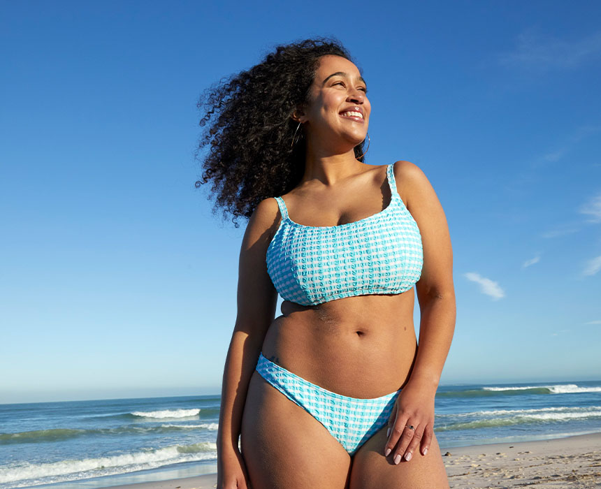 Femme souriante debout sur une plage avec la mer en arrière-plan