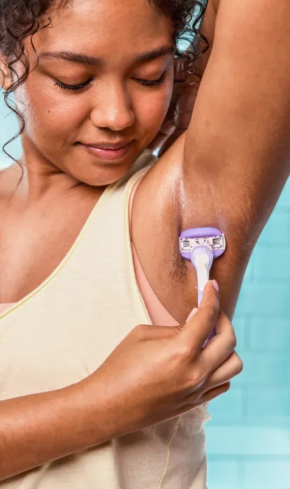 Jeune femme assise sur un tabouret dans la salle de bains, rasant son aisselle
