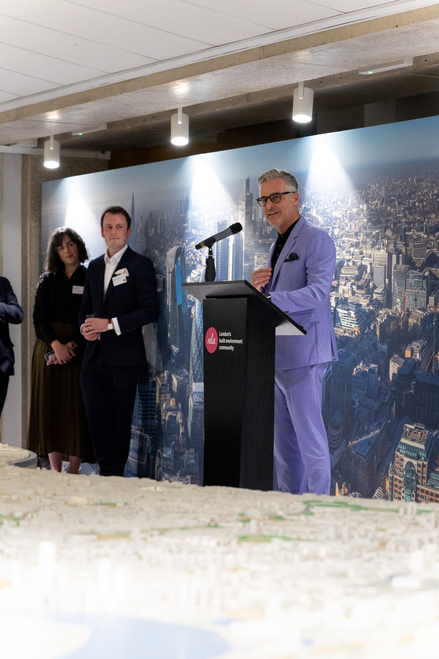Earle Arney talking from the lectern, looking over the London Model