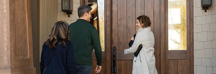 A relator walks a couple up to the front door of a home that has a lock box on the door handle